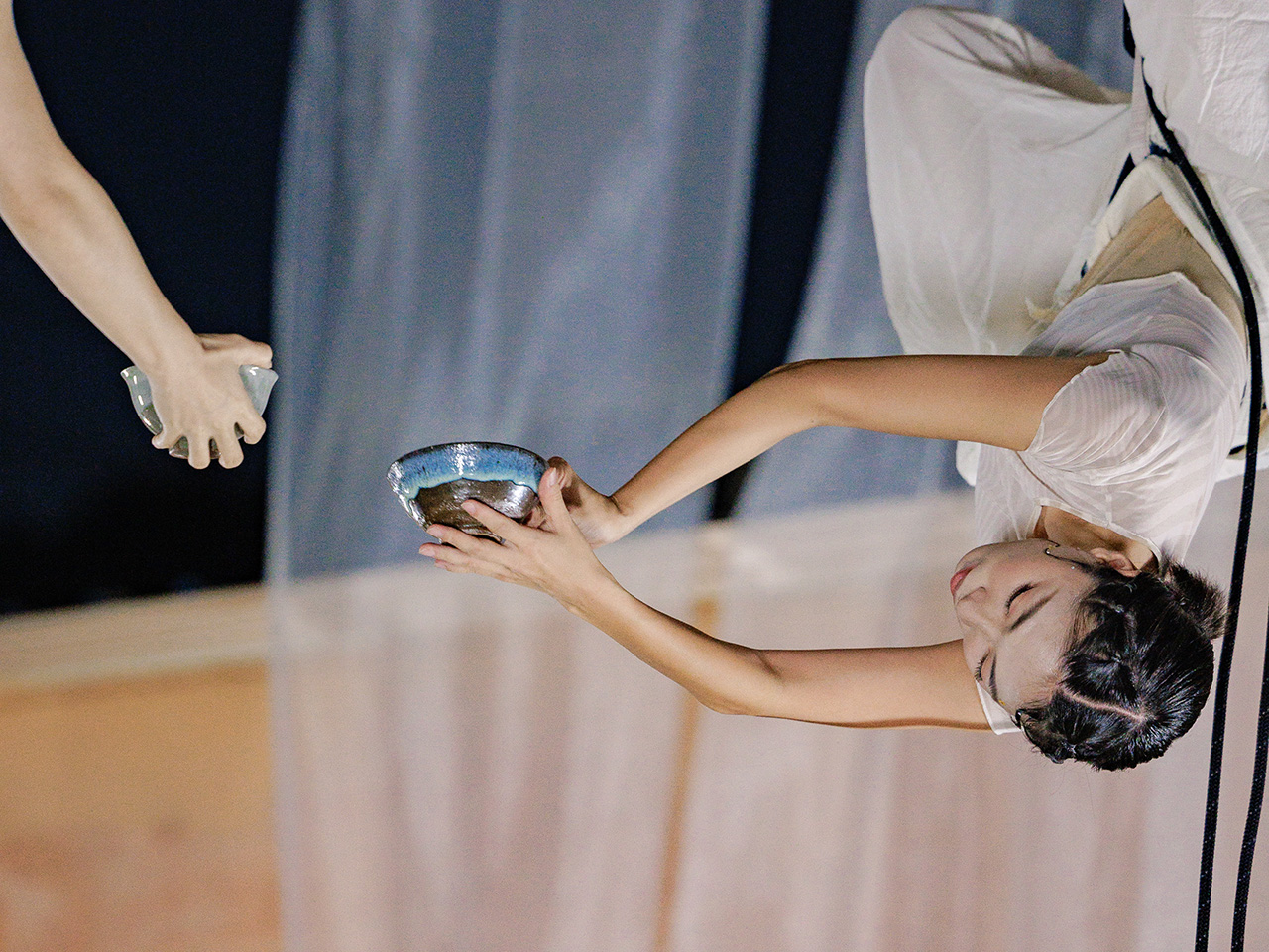 공중에 매달린 여성 무용수가 다른 사람에게 그릇을 건네는 퍼포먼스를 하고 있다.